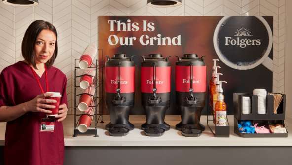 A woman standing next to a Folgers coffee bar