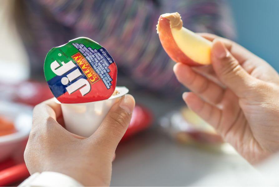 Close-up of someone holding a JIF Portion Control cup and dipping an apple slice into it.